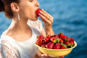 Woman eating fresh strawberry from a big yellow plate outdoors on the blue sea background