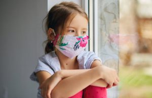 Little girl, child in mask sits on windows, coronavirus quarantine