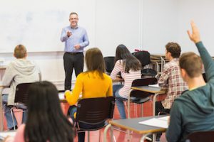 Rear view of students attentively listening to male teacher in the classroom