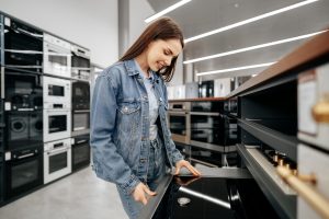 Young brunette woman choosing new electric stove in a hypermarket
